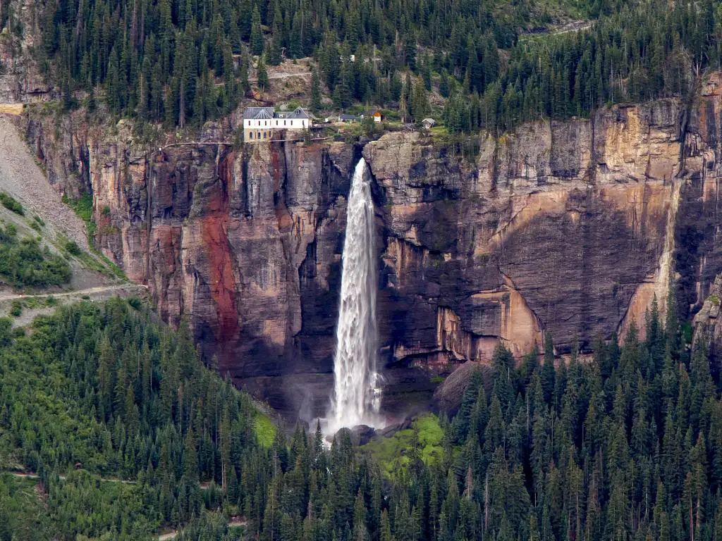 La cascada de flujo libre más alta de Colorado cae en cascada por una roca escarpada con pinos en las laderas circundantes