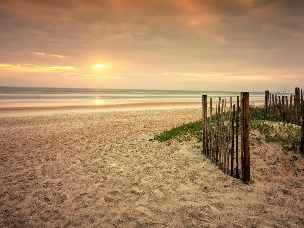 Ormond Beach, Florida, Estados Unidos, con una playa de arena, una cerca de madera y una puesta de sol lejana.