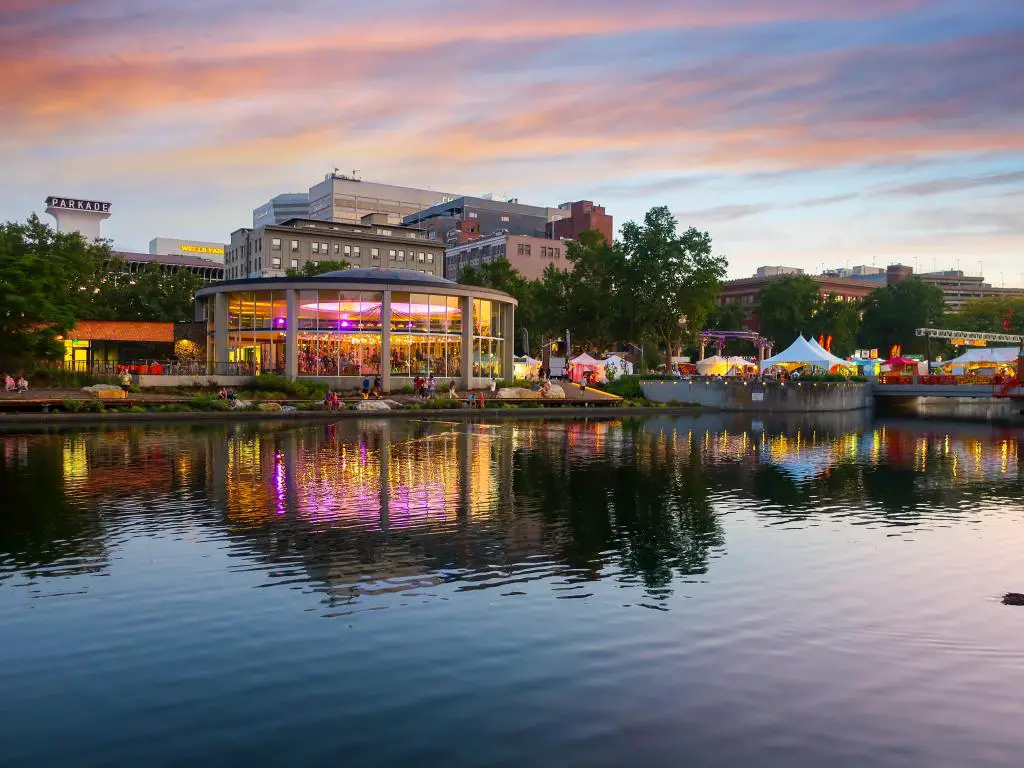 Spokane, Washington, EE.UU. tomada en el Looff Carousel, que está iluminado de colores y se refleja en el río junto con las carpas de comida del festival y las tiendas al atardecer durante el festival Pig Out in the Park.