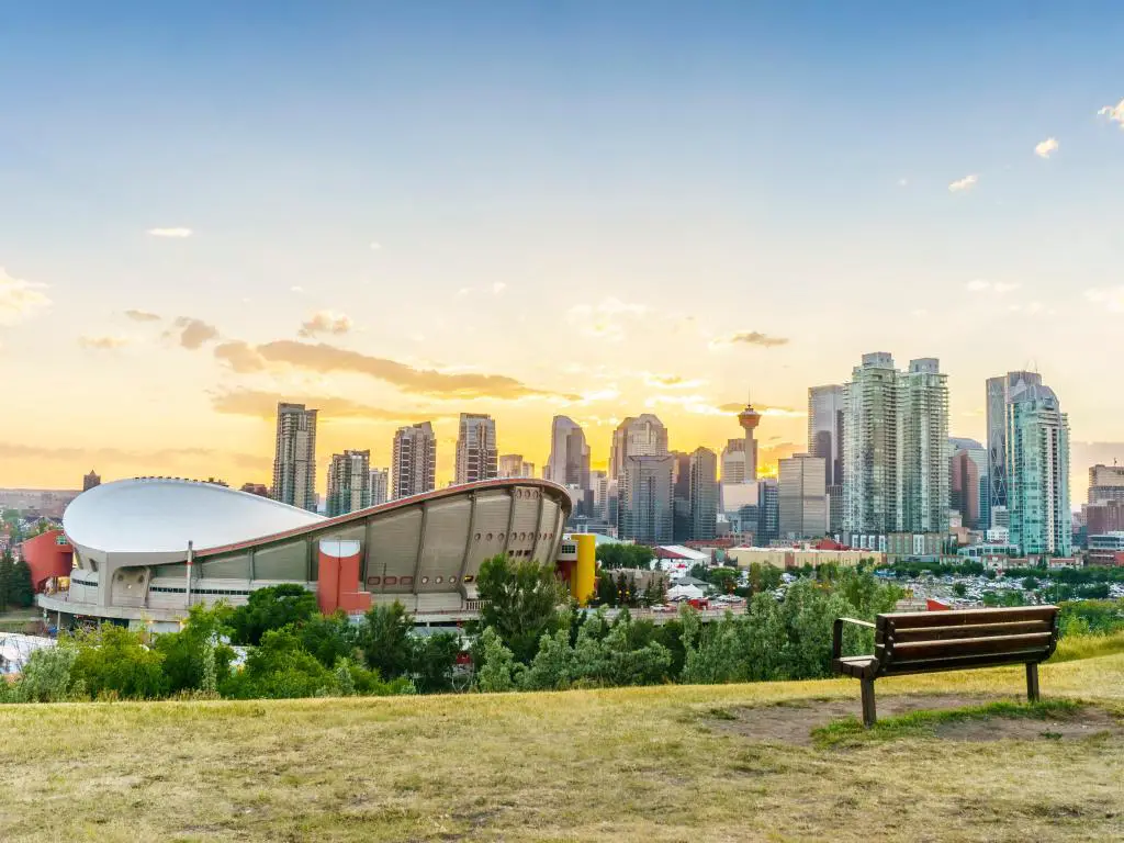 Calgary, Alberta, Canadá, con el centro de la ciudad al atardecer durante el verano, y un banco y un área de césped en primer plano.