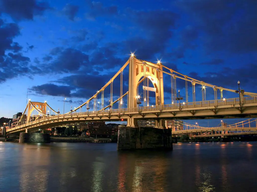 Puente que cruza el río Allegheny iluminado después del anochecer, con más puentes visibles al fondo