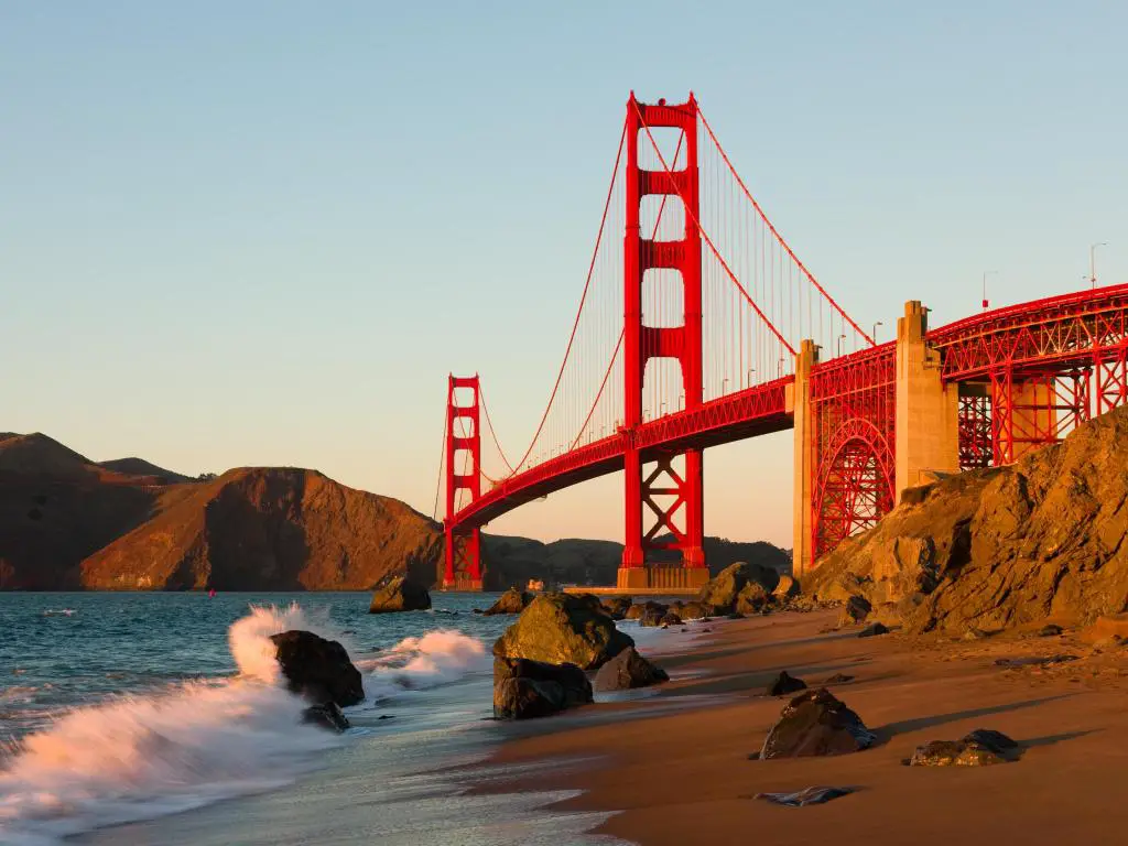 Puente Golden Gate en San Francisco al atardecer con olas rompiendo en la playa.