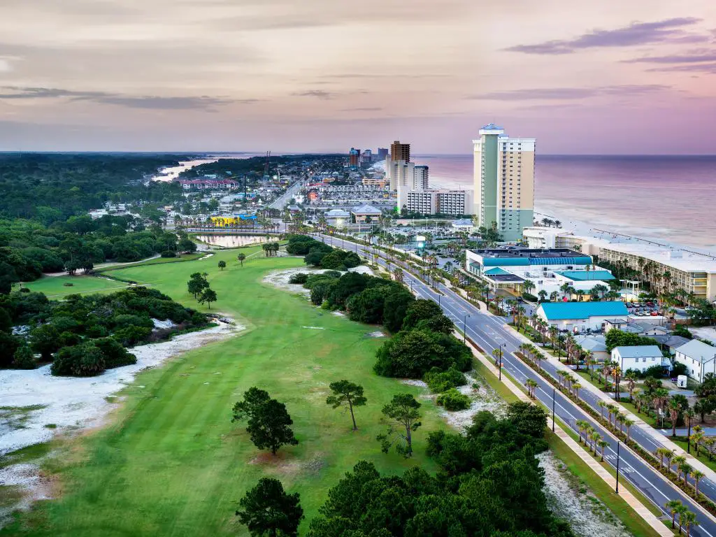 Panama City Beach, Florida, EE.UU. con vistas a Front Beach Road al amanecer con vegetación y árboles a un lado y la costa al otro.