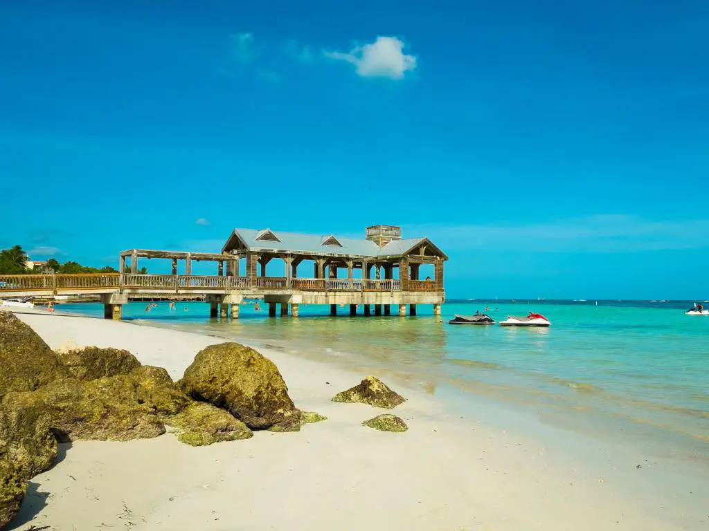 Key West, Florida Keys, EE. UU. Con una hermosa playa con un muelle cubierto a lo largo de la costa a lo lejos y aguas turquesas.