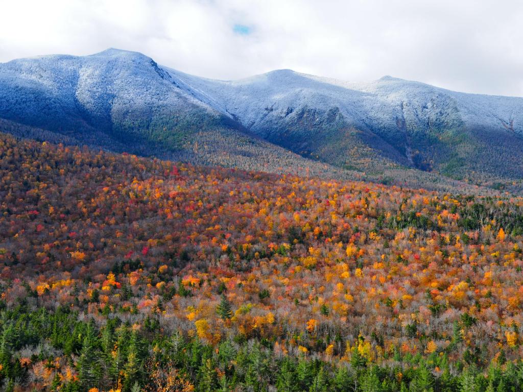 Las Montañas Blancas, New Hampshire, Estados Unidos, tomadas durante el otoño con amarillos y naranjas en el follaje en primer plano y nubes bajas sobre las montañas en la distancia.