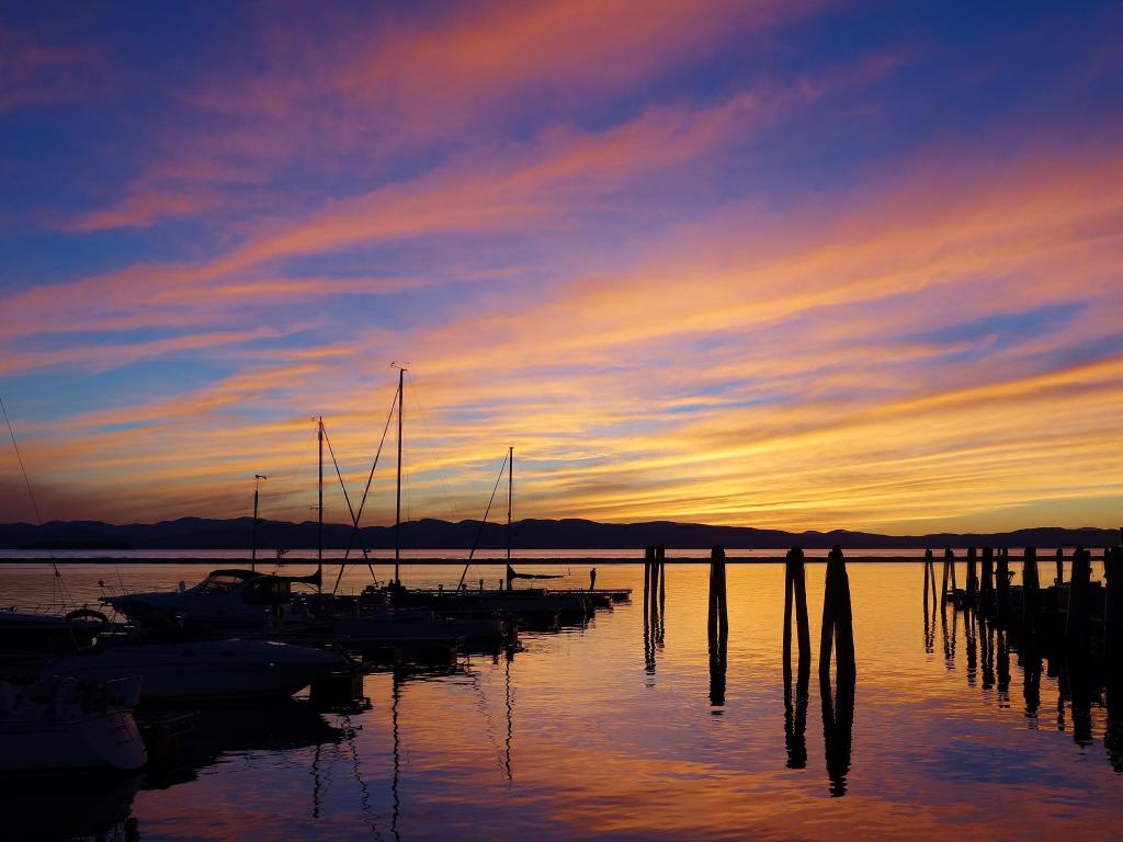 Lago Champlain, Burlington, Vermont, EE. UU. Tomado al atardecer con el impresionante cielo reflejado en el lago con tenues nubes naranjas reflejadas en el agua, barcos y un muelle en silueta.