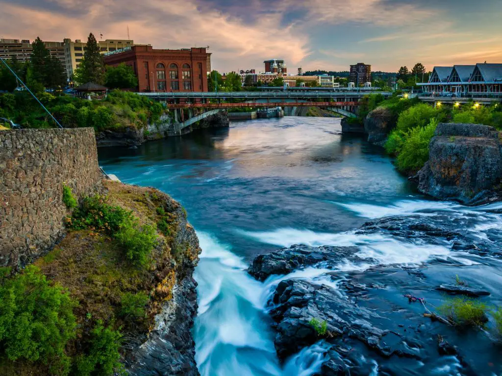 Spokane Falls, Spokane, Washington, EE. UU. Con la cascada en primer plano, un puente y edificios en la distancia tomada al atardecer. 