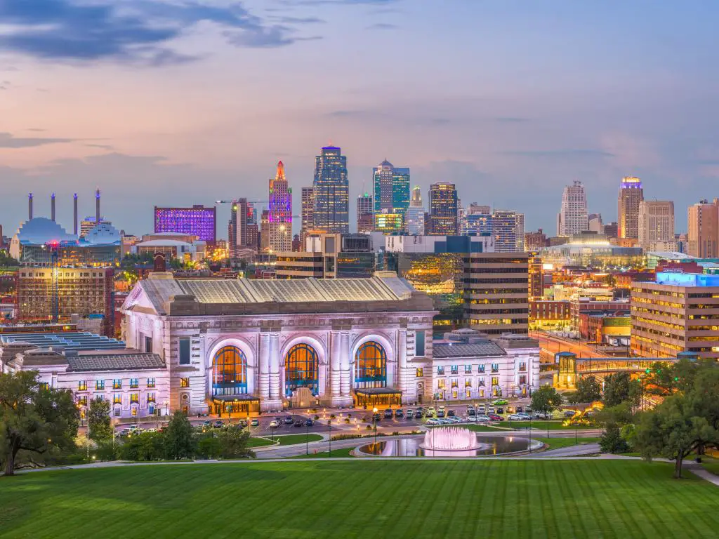 Kansas City, Missouri, EE.UU. tomada del horizonte del centro de la ciudad con Union Station al anochecer, una zona de césped verde en primer plano. 
