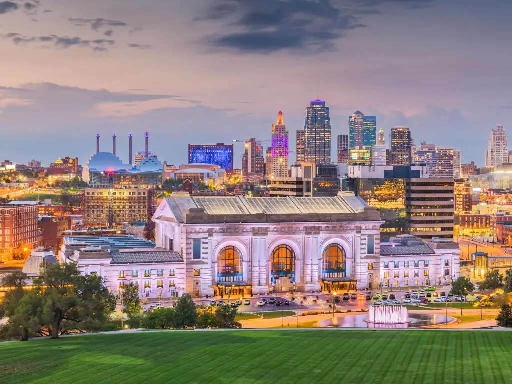 Kansas City, Missouri, con el horizonte del centro de la ciudad con Union Station al atardecer y hierba verde en primer plano. 