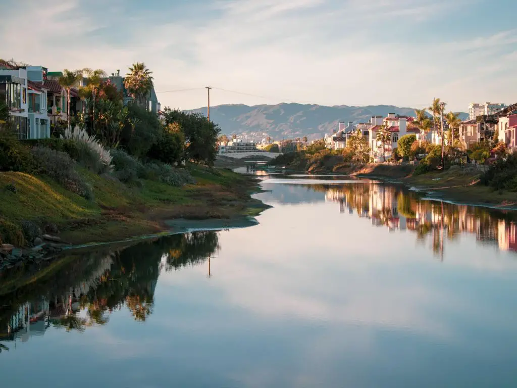 Gran Canal en Marina Del Ray, California, EE.UU. tomada al atardecer con el agua en primer plano, casas y hierba a ambos lados y colinas en la distancia. 