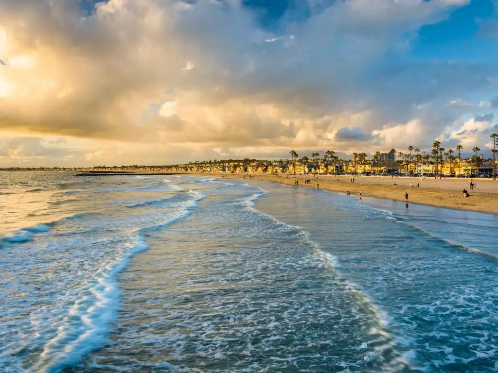 Newport Beach, California, EE.UU. con olas en el Océano Pacífico en primer plano y una vista de la playa al atardecer.