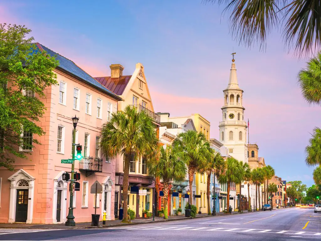 Charleston, Carolina del Sur, EE.UU. tomada en el Barrio Francés al atardecer con edificios bellamente pintados y una iglesia en la distancia, palmeras que bordean la calle.