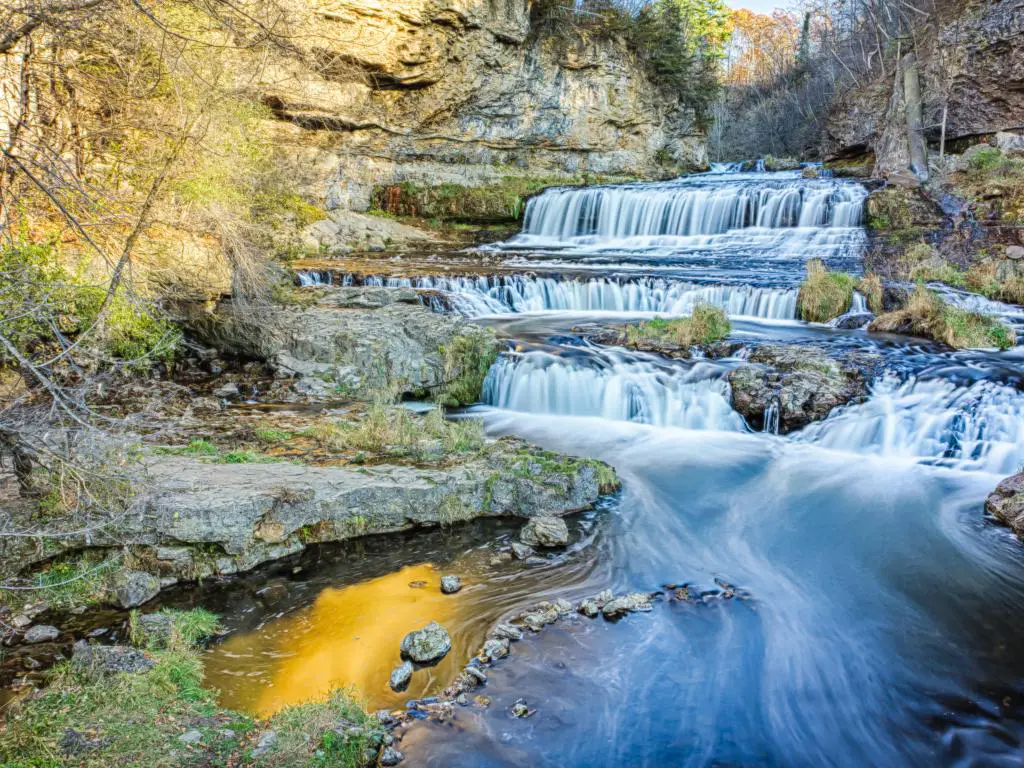 Willow River Falls, EE. UU. Tomado en un día de la tarde durante el otoño con pequeñas cascadas que conducen al agua en primer plano y terreno rocoso en la distancia. 