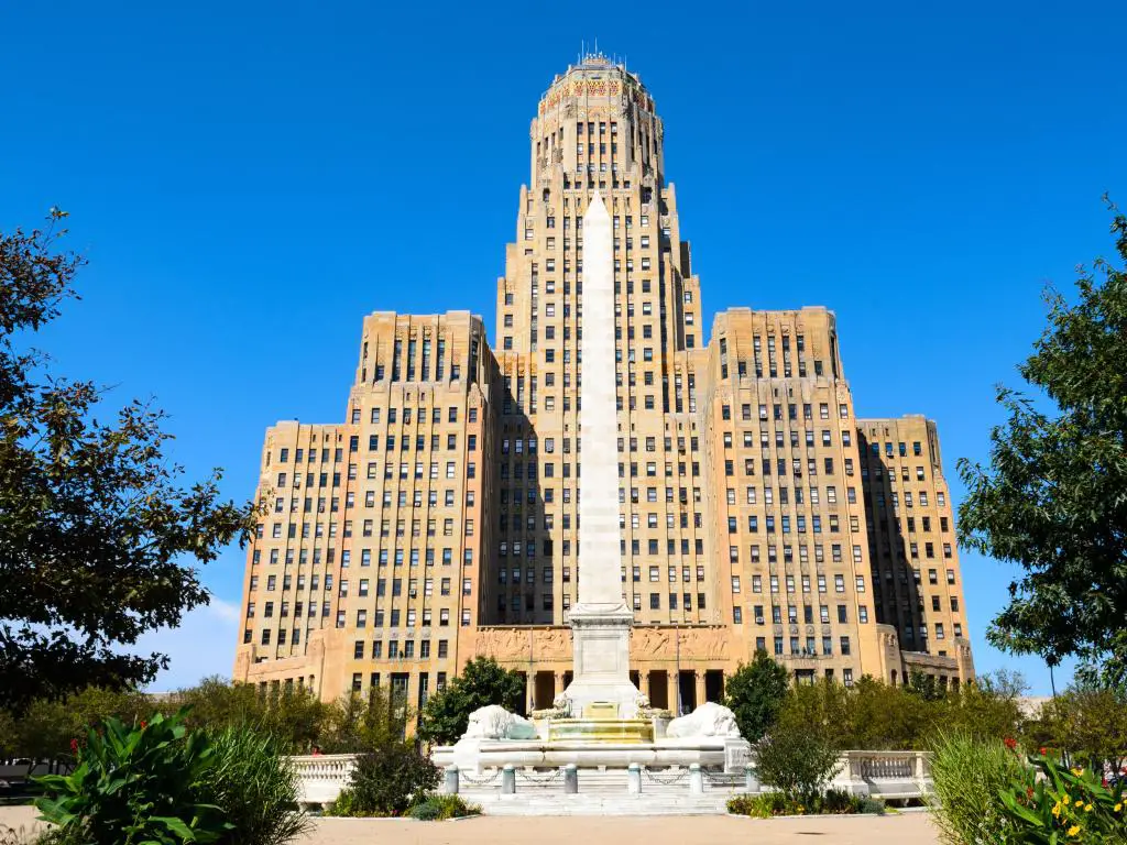 Ayuntamiento de Buffalo, Buffalo, EE.UU. con árboles y plantas en primer plano y el icónico edificio sobre un fondo azul brillante.