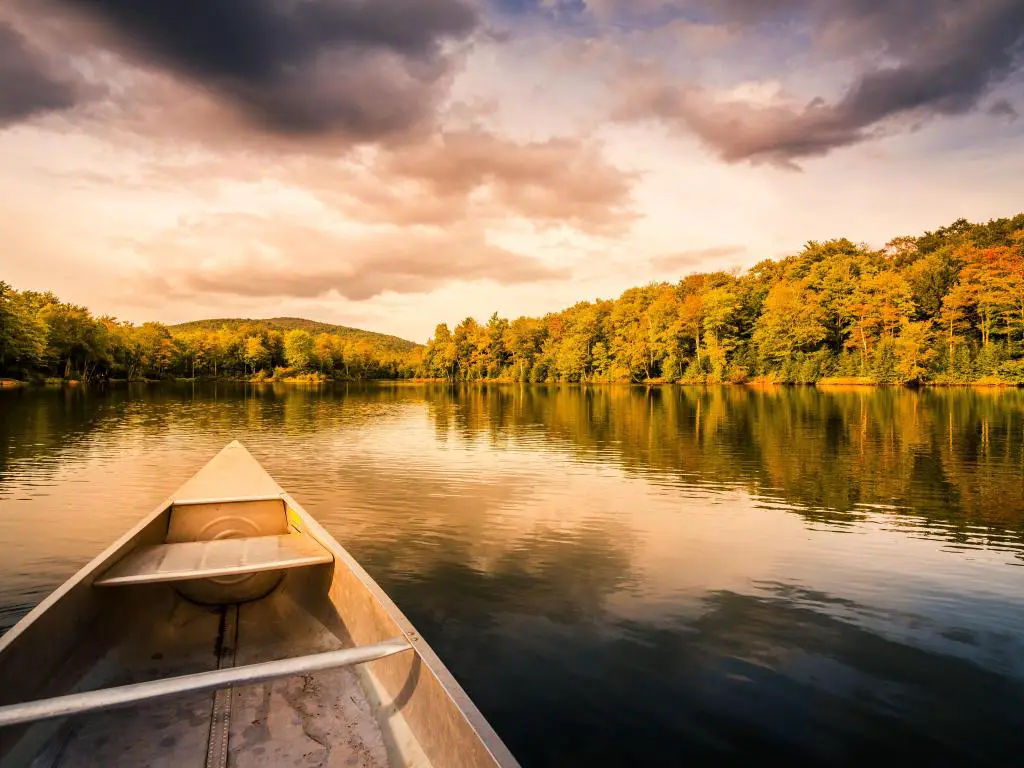 Canoa de aluminio en un lago de montaña con árboles que bordean las orillas y un cielo nublado