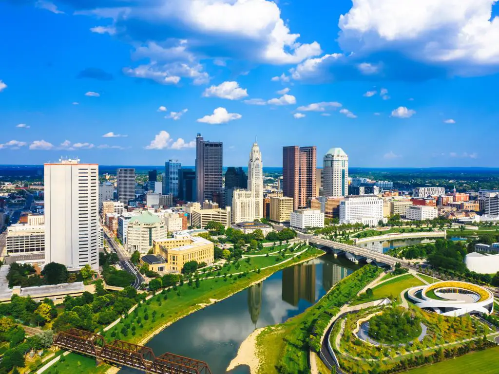 Vista aérea del centro de Columbus Ohio con el río Scioto.  El cielo es azul con algunas nubes y hay un parque en el primer plano de la foto.