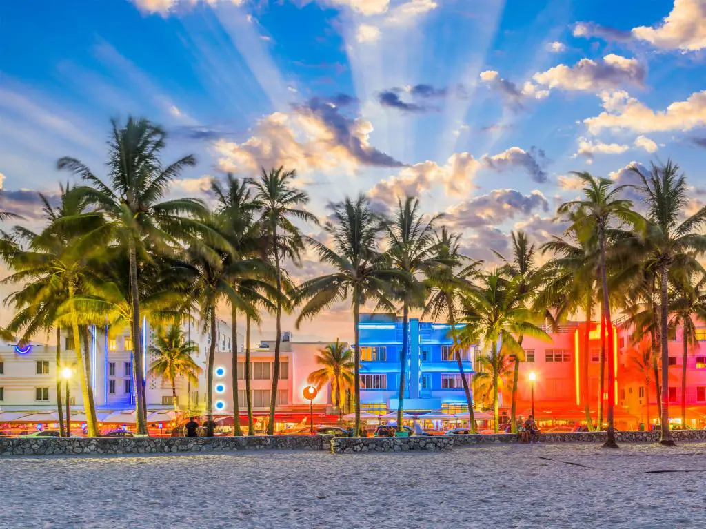 Playa con palmeras y edificios de colores brillantes con rayos de luz del sol poniente detrás de ellos