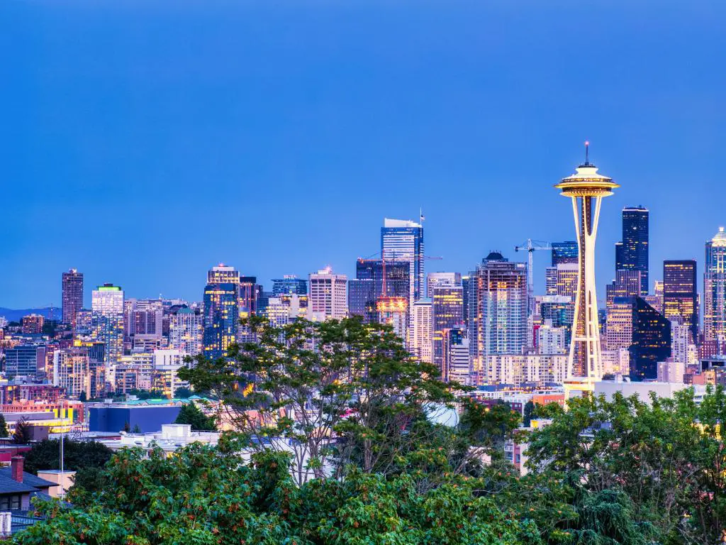 Seattle, Washington, EE. UU. con el paisaje urbano y el Monte Rainier al fondo y tomada al atardecer con algunos árboles en primer plano. 