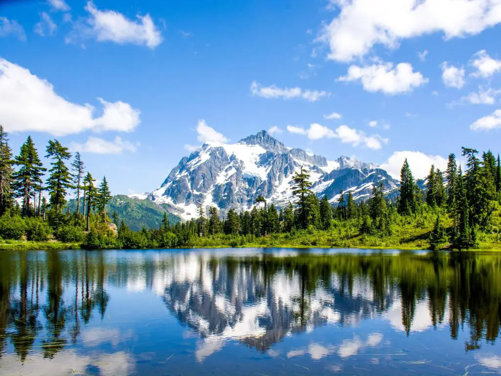 Parque Nacional North Cascades, Washington, EE.UU. con el paisaje del Monte Shuksan reflejado en el lago Picture en primer plano y rodeado de árboles en un día soleado. 