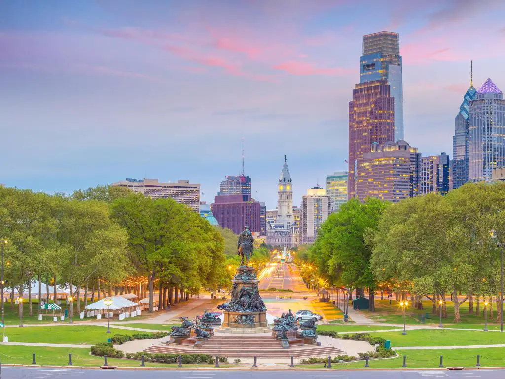 Filadelfia en Pensilvania, Estados Unidos, con el paisaje urbano del centro de la ciudad al fondo y un parque verde y un monumento en primer plano tomados al atardecer.