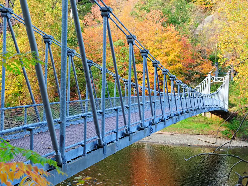 El puente peatonal se extiende sobre un valle empinado con follaje otoñal rojo, dorado y verde 