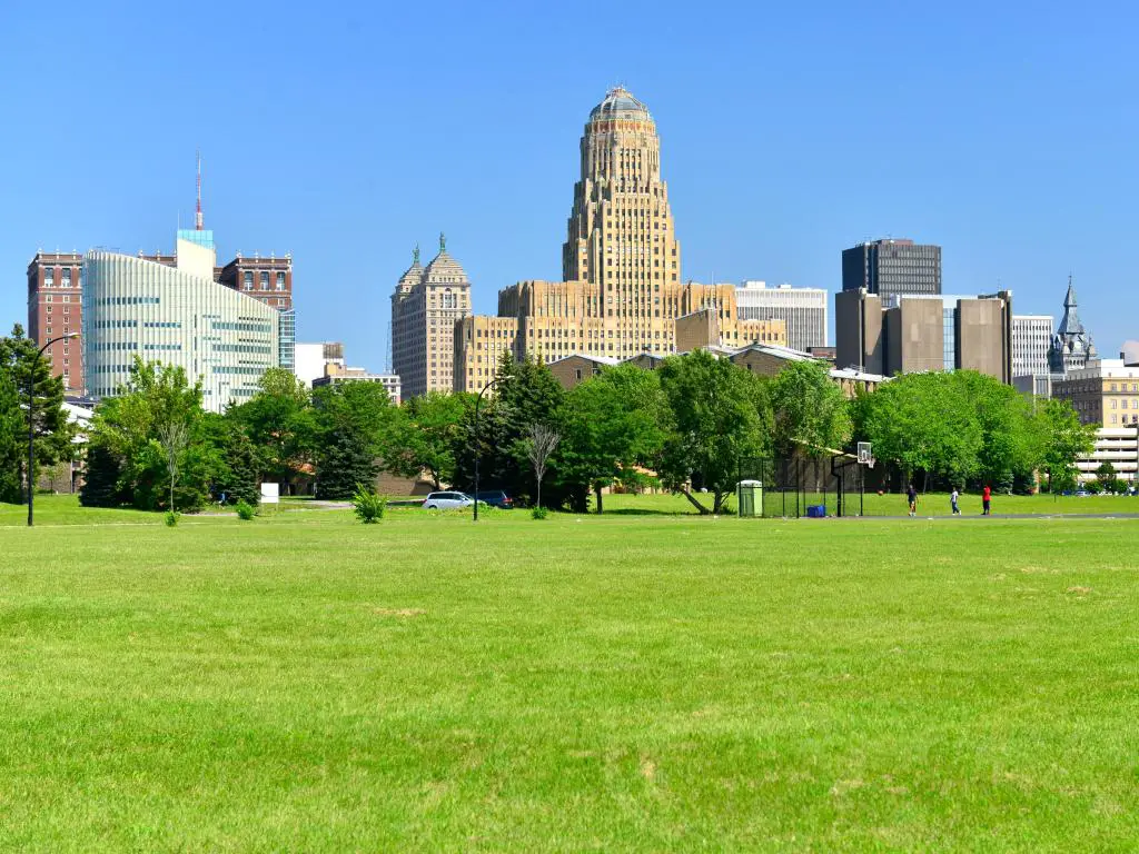Buffalo, Nueva York, Estados Unidos, con un parque verde en primer plano, árboles y el horizonte de la ciudad a lo lejos en un día claro y soleado.