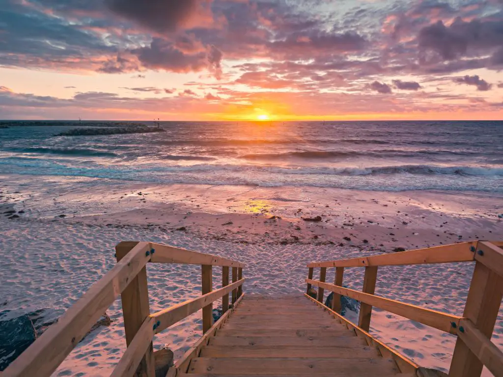 Puesta de sol sobre el océano con escalones de madera que conducen a una playa de arena en primer plano