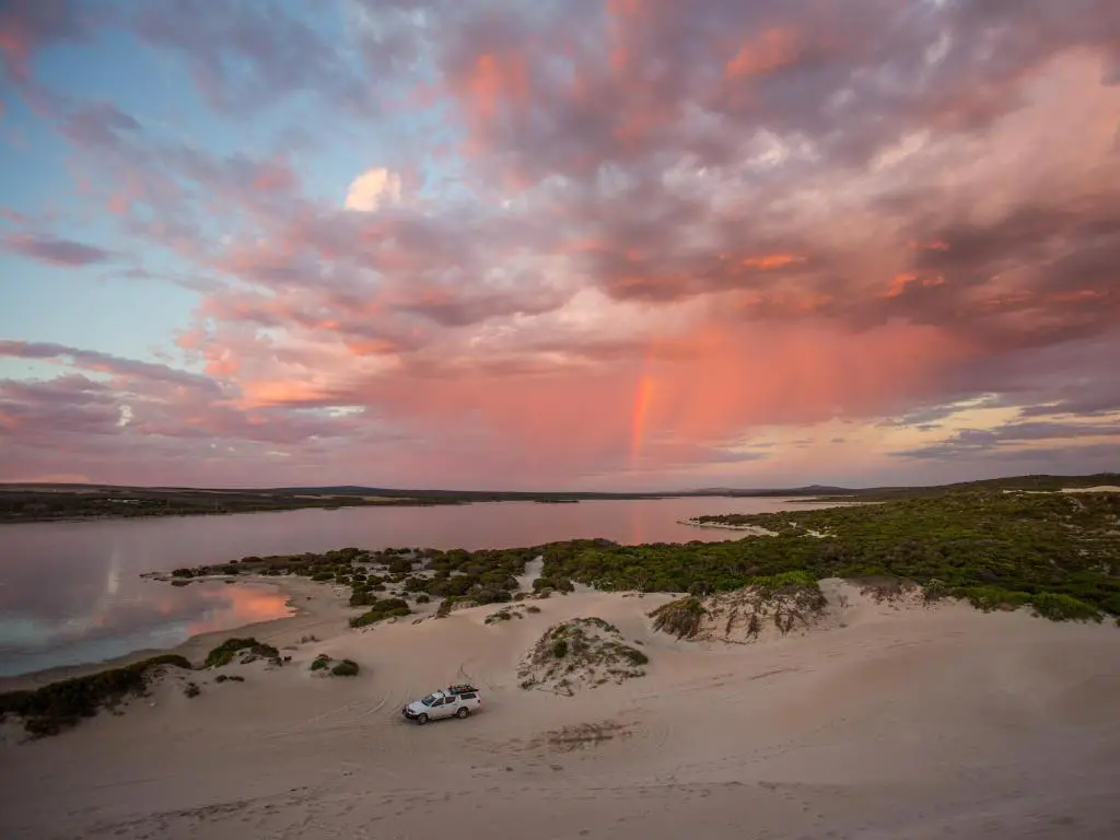 Playa de arena y aguas tranquilas que reflejan el cielo rosa del atardecer