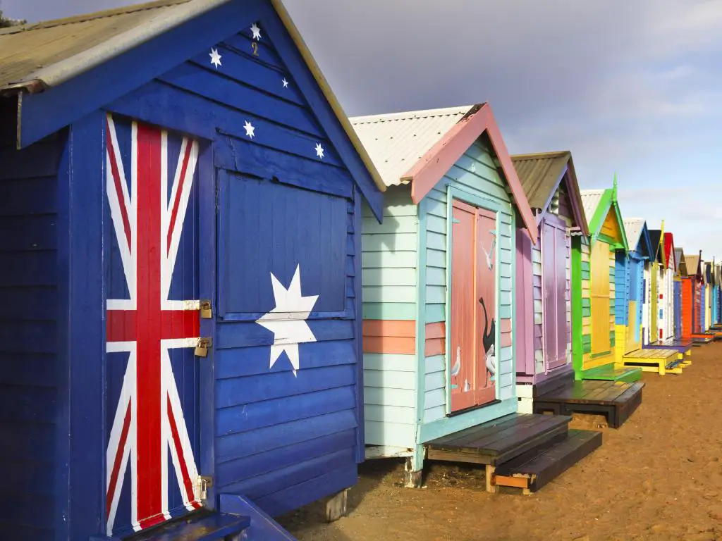 Casas de playa pintadas en colores vibrantes en una playa de arena, incluida una en la bandera australiana