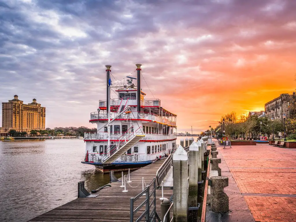 Paseo frente al río al amanecer con cielo rosa y barco antiguo rojo y blanco amarrado por el paseo marítimo
