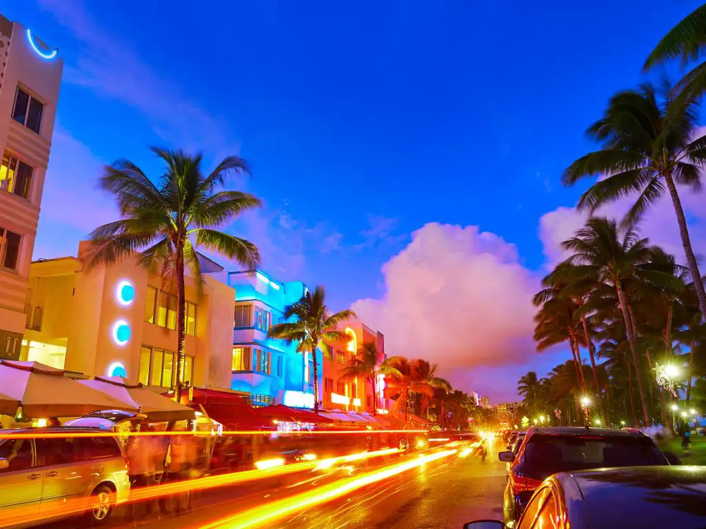 Edificios Art Deco iluminados en colores neón con luces de auto y palmeras