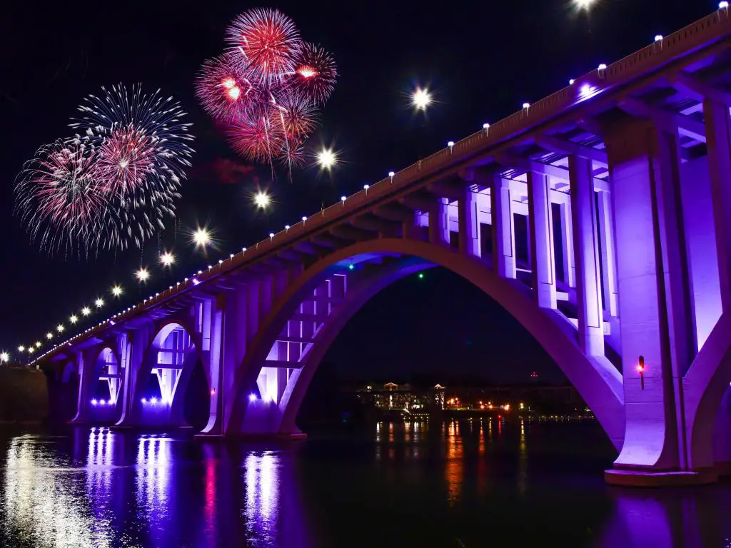 Puente sobre el río ancho iluminado por la noche con grandes fuegos artificiales