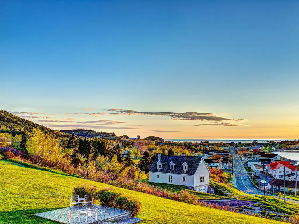 Perce, Península Gaspe, Quebec, Canadá con sillas en la colina en primer plano tomadas durante el amanecer en Perce, y el paisaje urbano en el fondo.