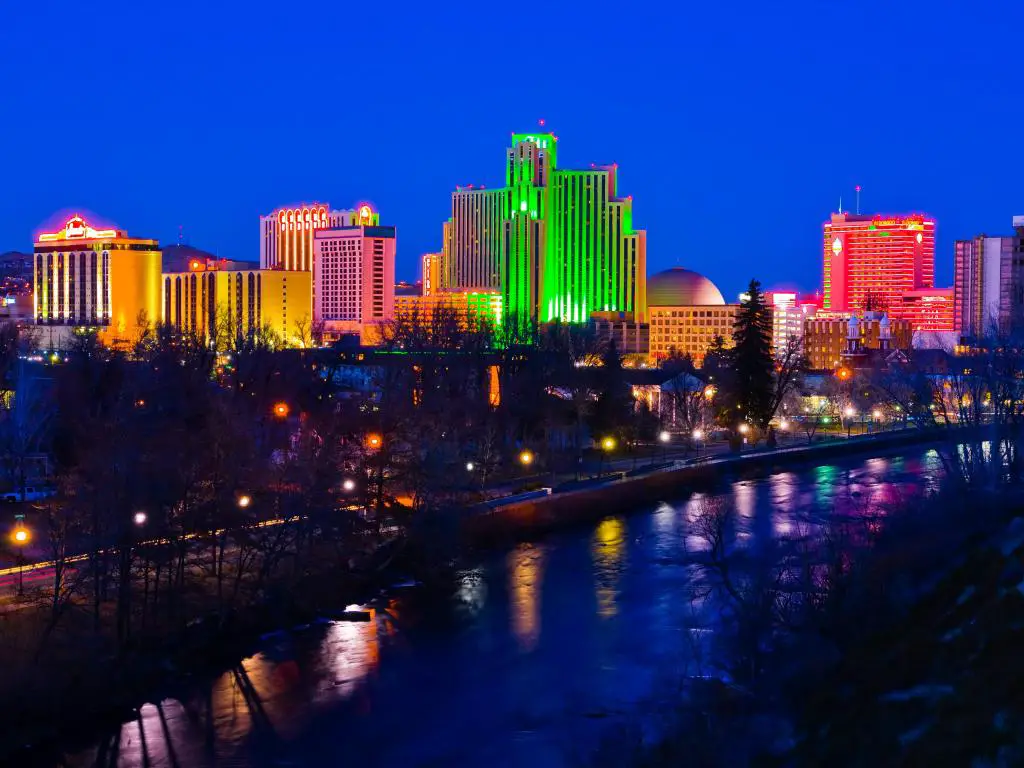 La colorida ciudad de Reno por la noche.  Los edificios están iluminados con luces de colores neón que se reflejan en el agua.