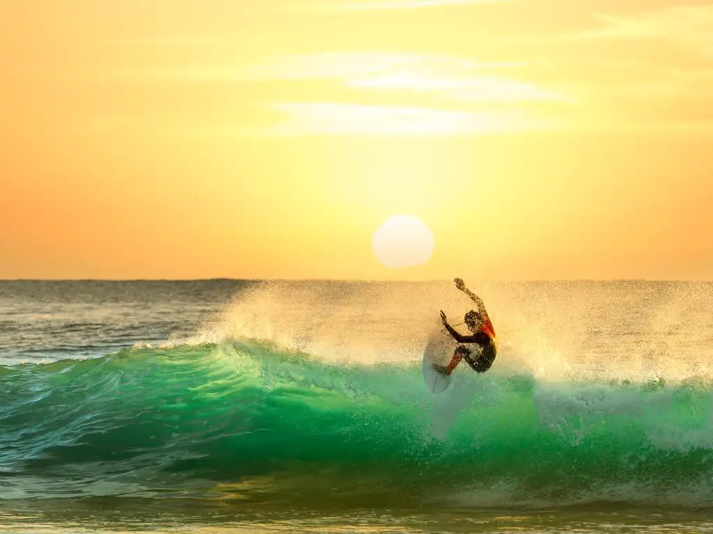 Surfista montando una ola con el sol poniente iluminando el agua