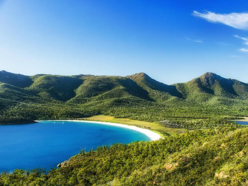 Tasmania, Australia en un día despejado, con montañas al fondo y un mar en calma en una bahía en primer plano. 