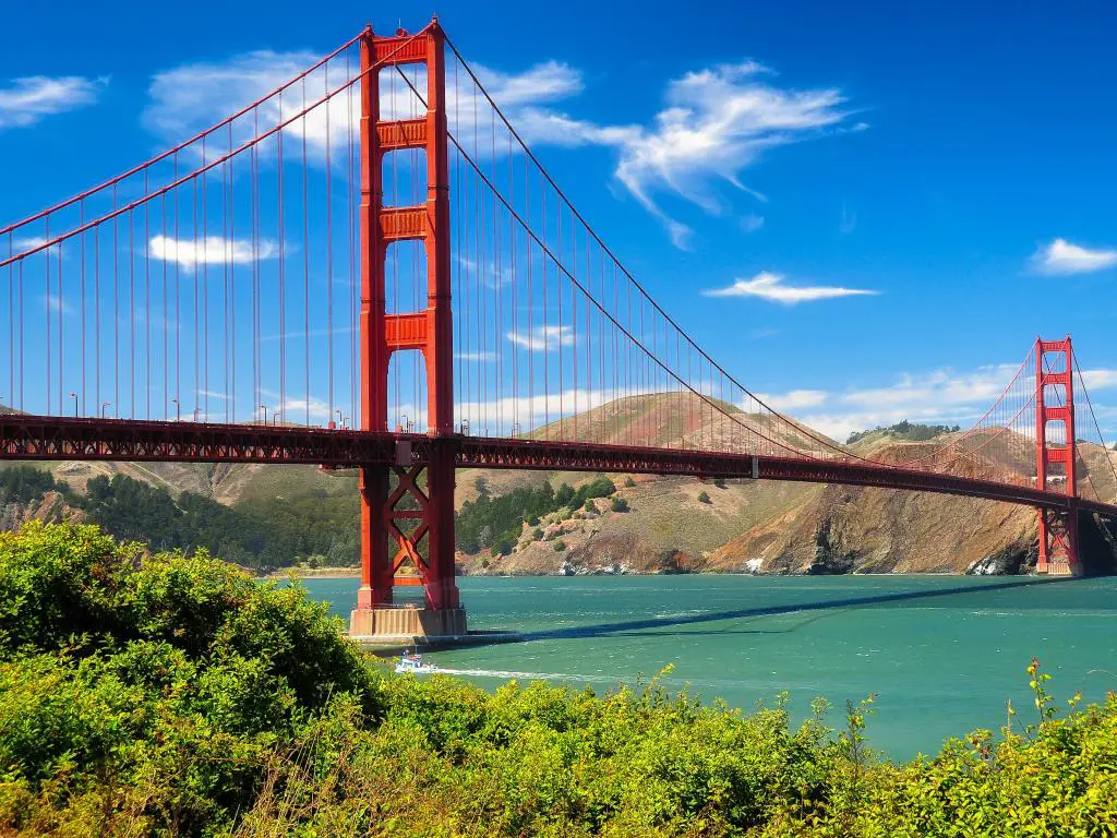 Estructura roja del puente Golden Gate que cruza aguas turquesas con cielo azul y vegetación verde vívida en primer plano