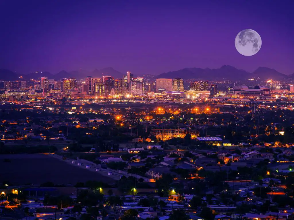 Vista del centro de Phoenix después del anochecer con una gran luna y luces de la ciudad que se reflejan en el agua