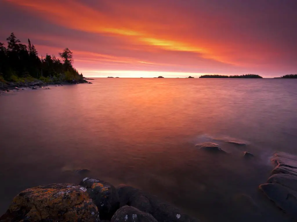 Parque Nacional Isle Royale, Michigan, tomada en Rock Harbor al amanecer con el cielo reflejándose en el agua en primer plano. 