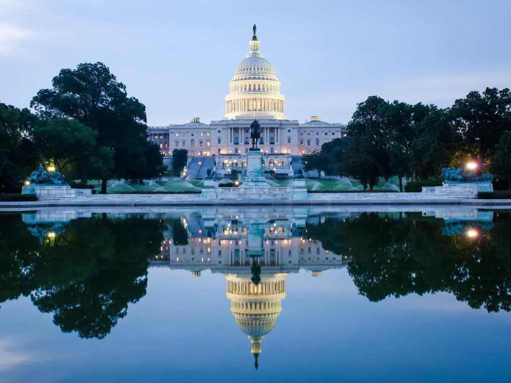 Reflejo del edificio del Capitolio de los Estados Unidos en aguas tranquilas al amanecer con árboles