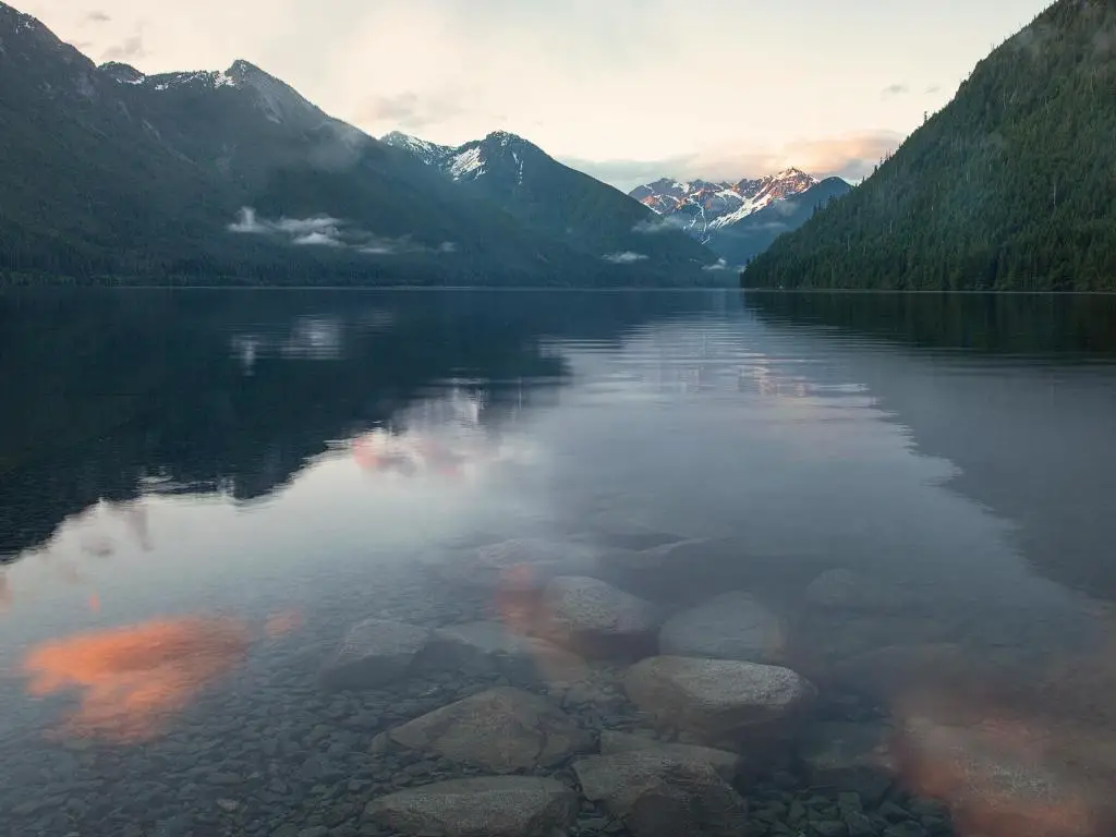 Chilliwack Lake, BC Canadá tomada durante un cálido amanecer sobre el tranquilo lago con montañas en la distancia reflejándose en el agua.