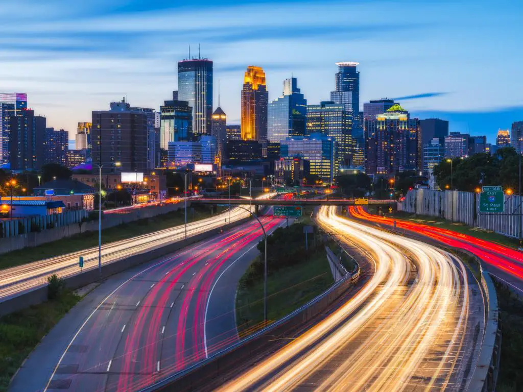 Minneapolis, EE.UU. con el horizonte de la ciudad a lo lejos y los semáforos de noche en primer plano creando una luz brillante en la carretera. 