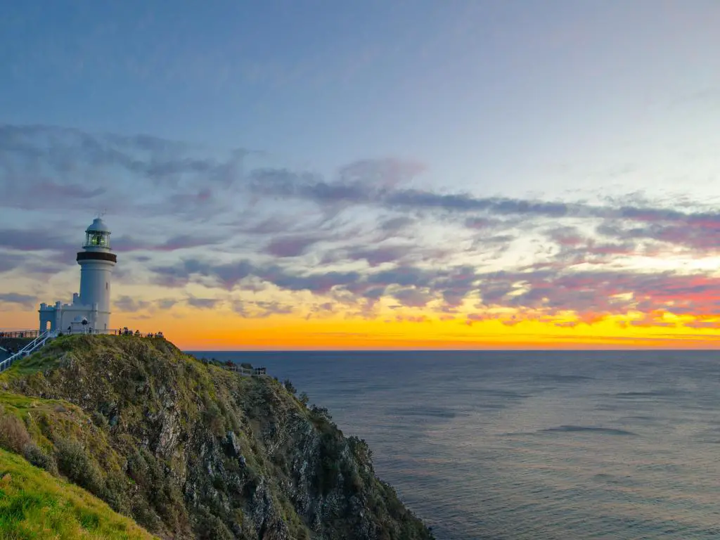 Faro en un acantilado con vistas al mar en calma con luz dorada y rosa del amanecer en el horizonte