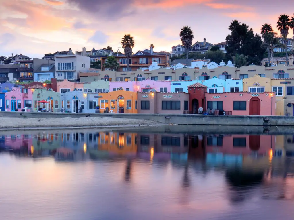 Edificios coloridos reflejados en aguas tranquilas, con cielo de puesta de sol gris y rosa y palmeras