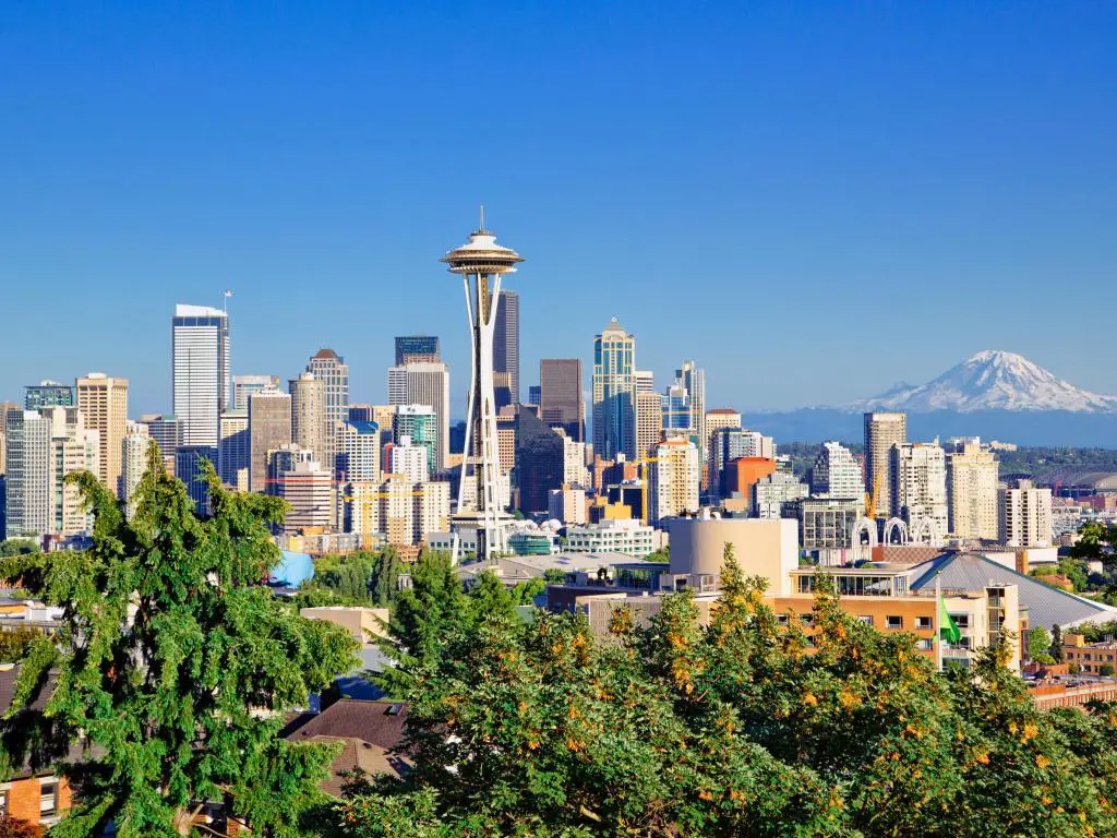 Seattle, Estados Unidos con el horizonte de la ciudad y los árboles en primer plano y el Monte Rainier en la distancia en un día despejado.