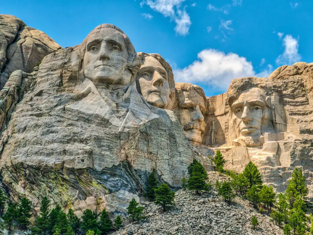 Monte Rushmore, EE. UU. con los rostros de los ex presidentes estadounidenses tallados en Black Hills, árboles en primer plano en un día soleado.