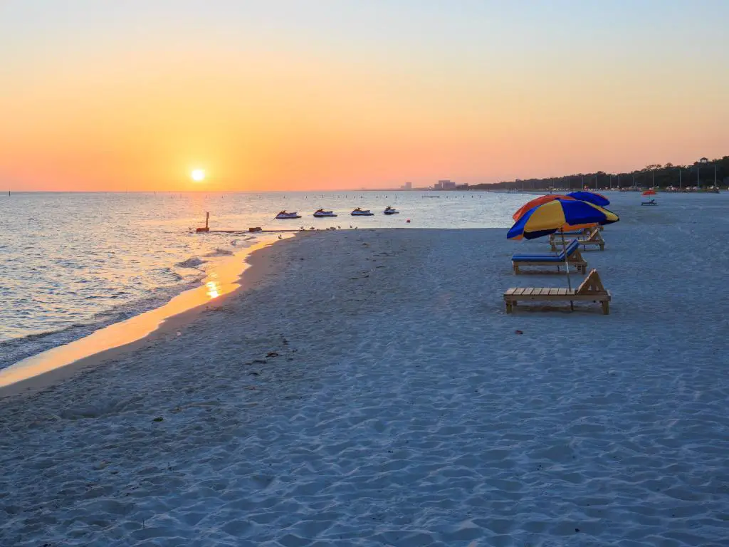 Playa de Biloxi, Mississippi al atardecer con vistas a la costa del Golfo con rayos de sol y sombrillas en una playa vacía.