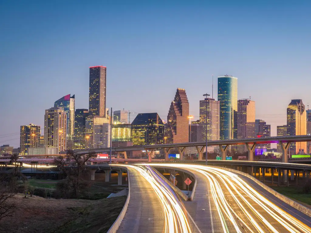 Houston, Texas, EE.UU. El centro de la ciudad y la autopista por la noche, con los edificios a lo lejos y la carretera en primer plano iluminada.
