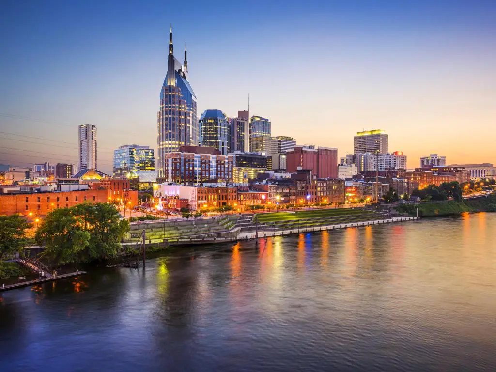 Nashville, Tennessee al atardecer con el horizonte de la ciudad iluminado y con vistas al río en primer plano. 