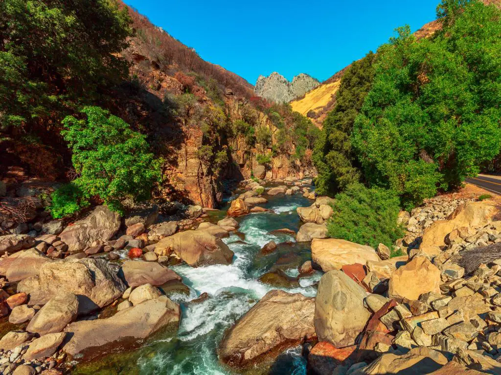 El río de agua blanca fluye a través de un canal rocoso con rocas de color naranja y un camino que bordea